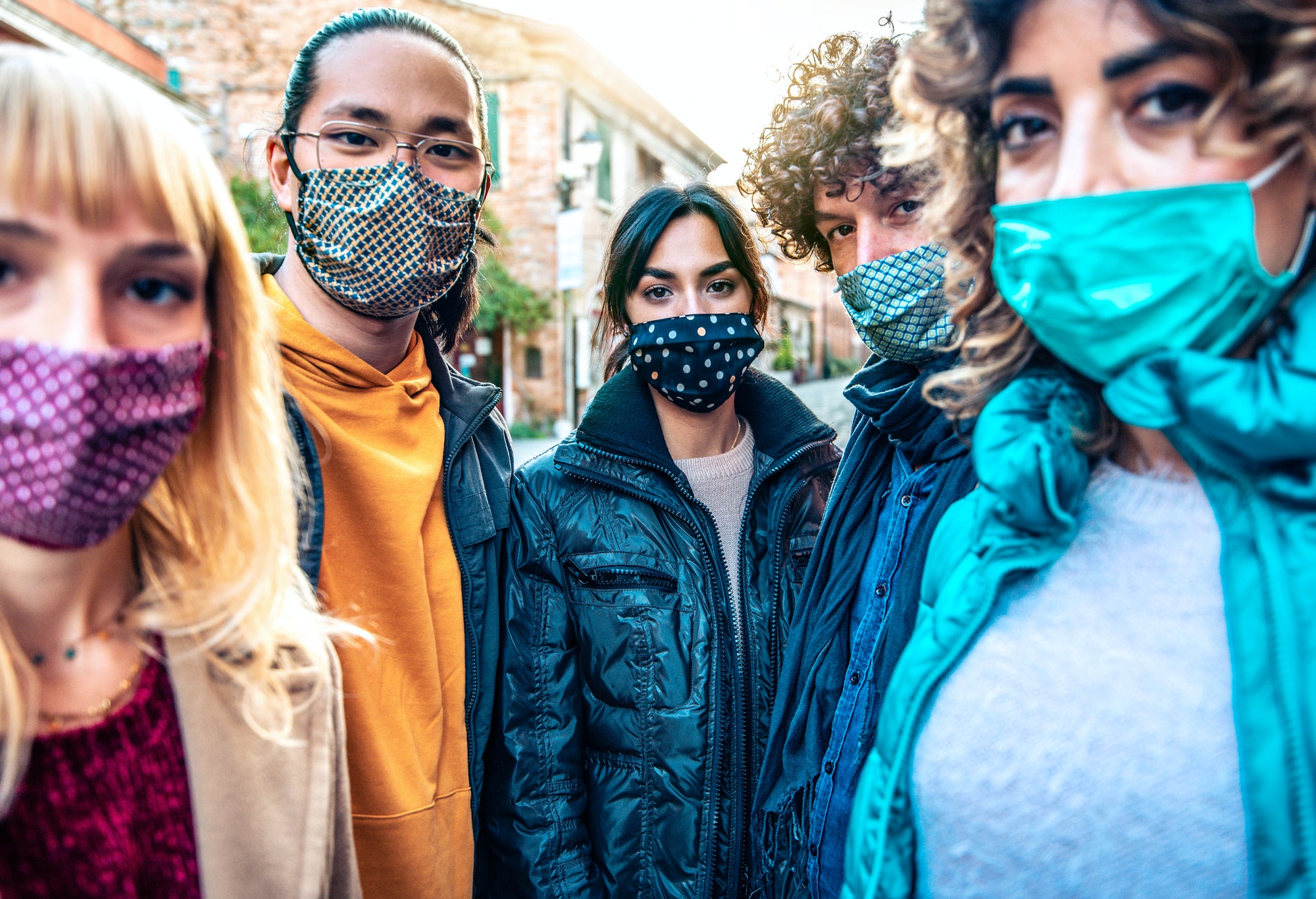 Community of multiracial people covered by facemasks looking at camera outdoors